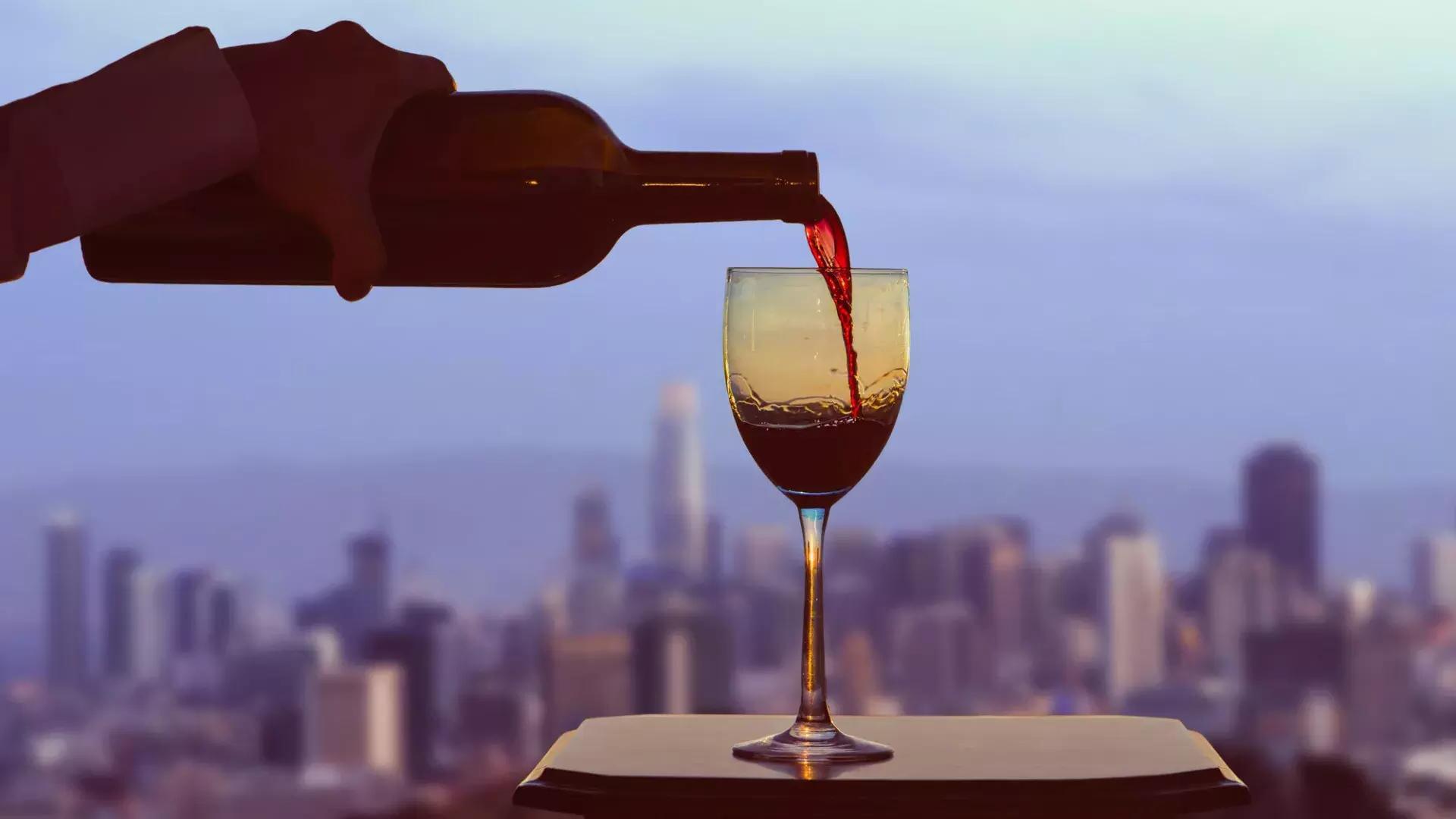 Se sirve una copa de vino tinto, con el horizonte de San Francisco visible desde la ventana.