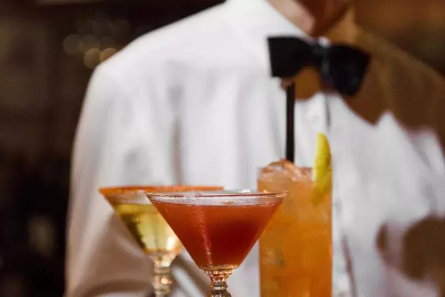 在贝博体彩app的苦艾酒餐厅，一名戴着领结的服务员展示一盘鸡尾酒.