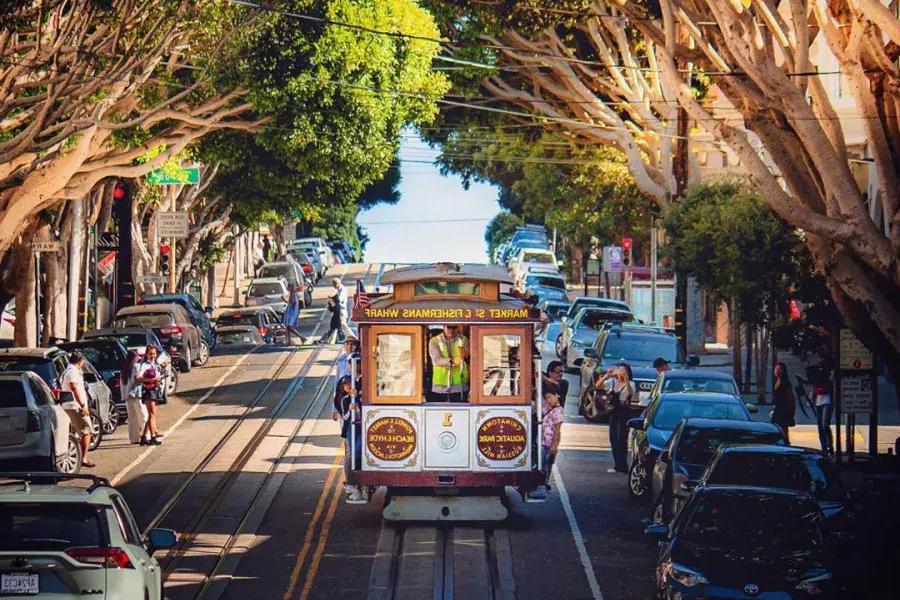 A San Francisco cable car approaches on a tree-lined street.