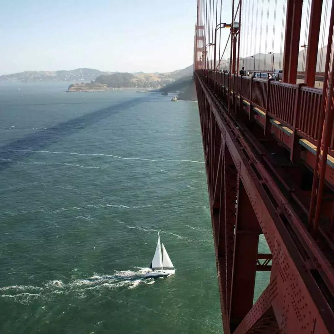 A small sailboat passes beneath the Golden Gate Bridge in the San Francisco Bay.