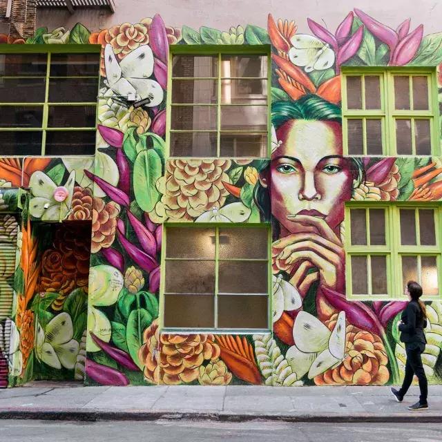 A woman looks up at a brightly colored mural on the side of an ornate building in San Francisco.