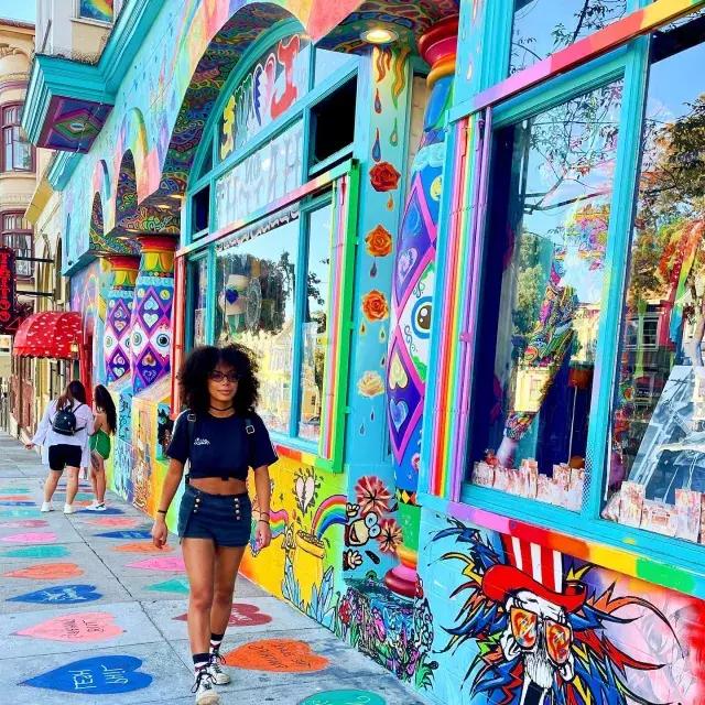 Mujer caminando por Haight Street con un colorido mural de fondo.